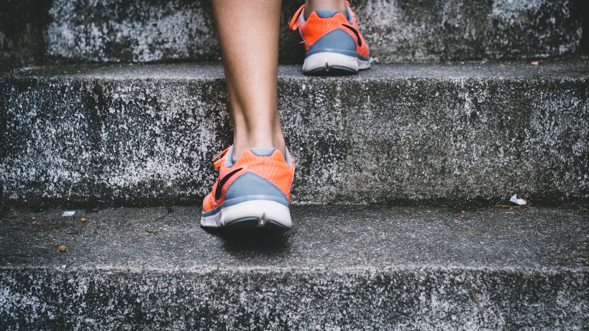 person wearing orange and gray Nike shoes walking on gray concrete stairs